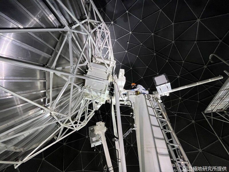 昭和基地の衛星通信「インテルサット」アンテナ（直径7.6m）のメンテナンス中。安全帯を装着し、高所で作業します
